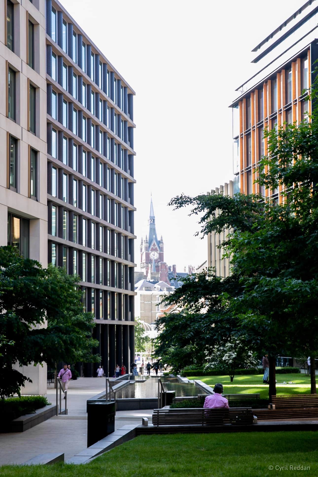 View of public space between tall buildings of Kings Cross with a church in the distance